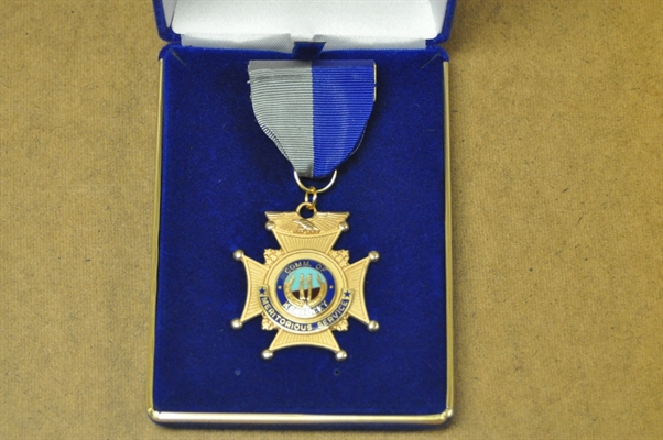 A gold medal with a blue and gray ribbon and a central emblem, displayed in a blue velvet case.