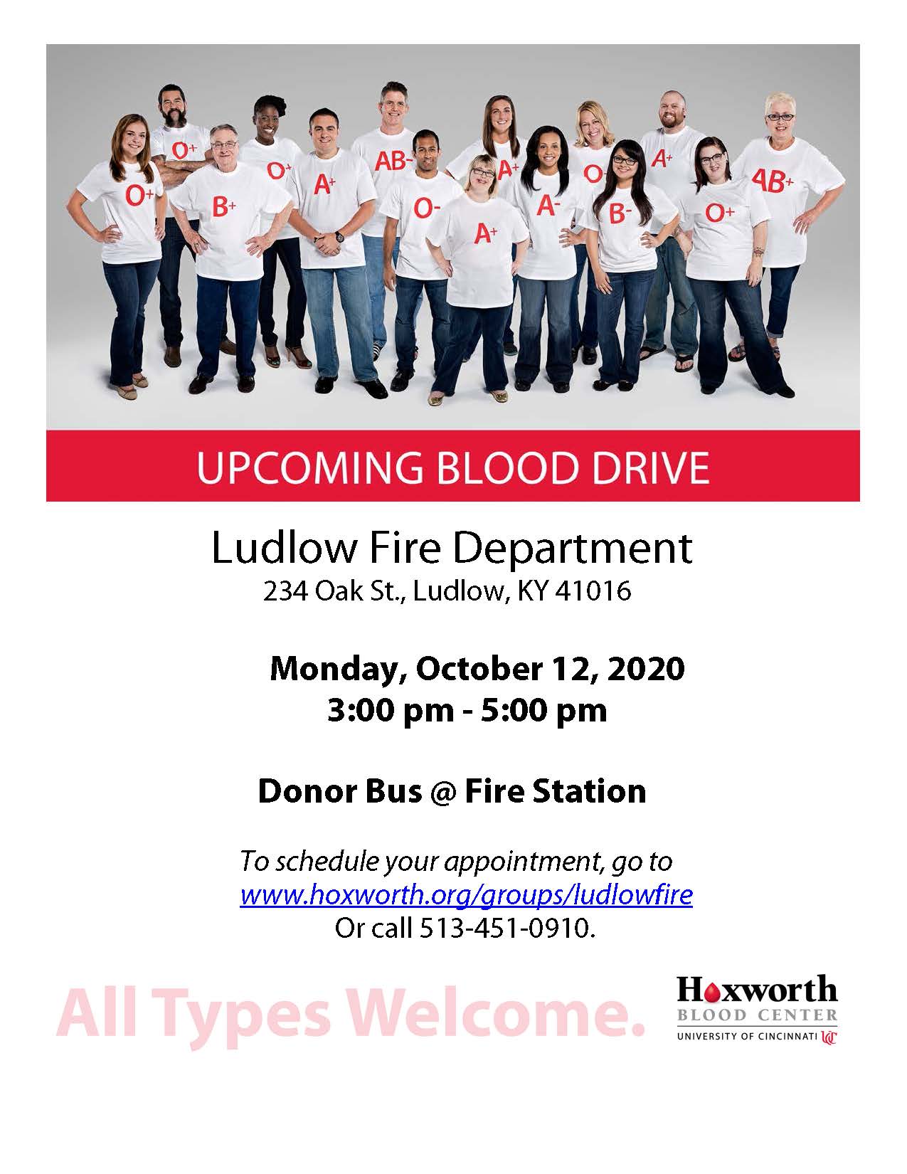 Group of people wearing shirts with blood types stand together under a banner for an upcoming blood drive at Ludlow Fire Department.
