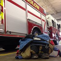 Firefighter gear placed on the floor next to a parked fire truck inside a fire station.