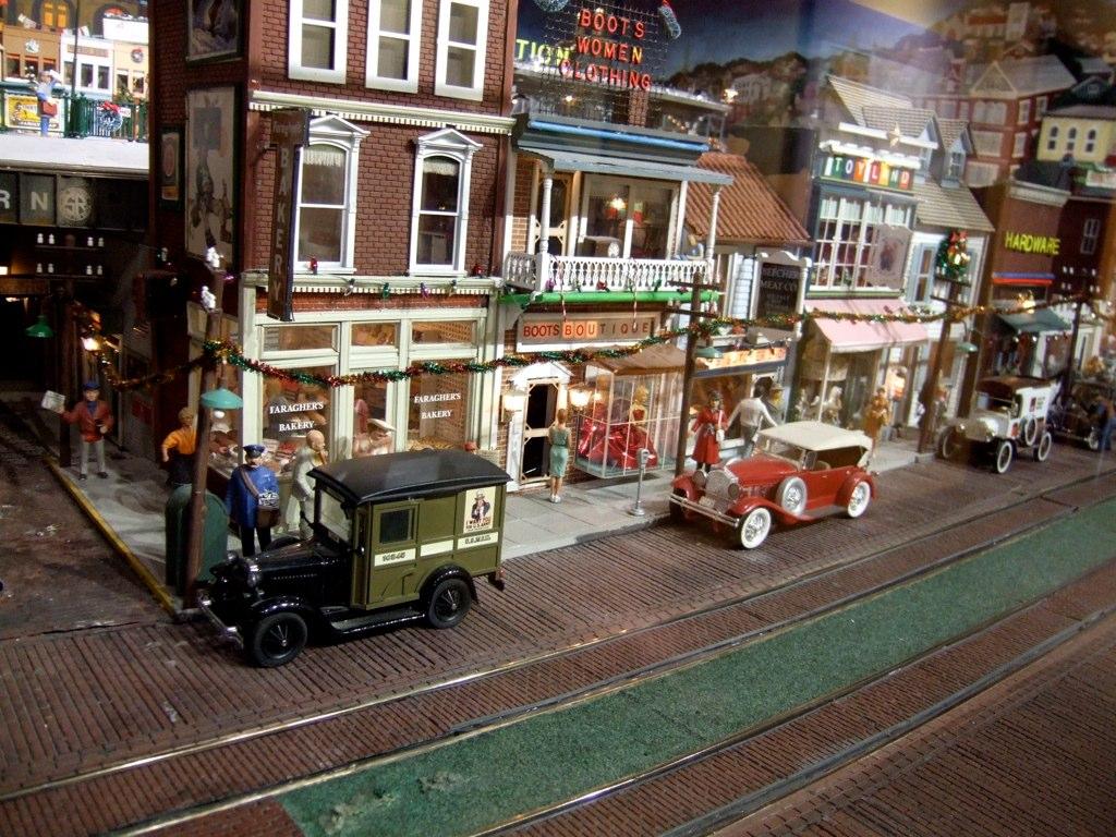 Miniature vintage street scene with model buildings, vehicles, and figures depicting a historical city block.