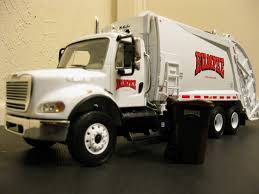White toy garbage truck with red logo parked on a surface next to a small black trash bin.