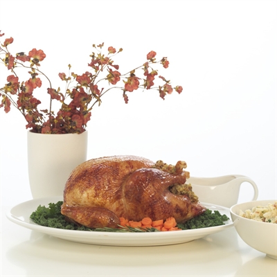 Roasted turkey on a platter with stuffing, surrounded by greens and carrots, next to a white bowl and floral vase.