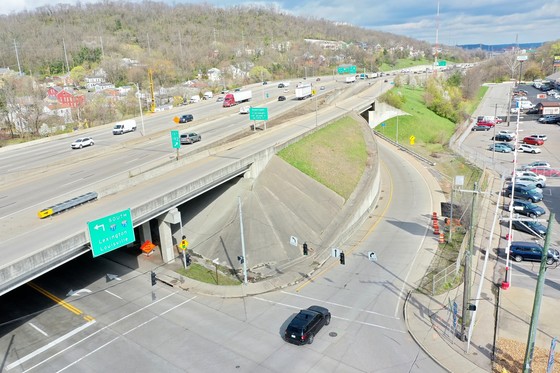 Aerial view of a multi-lane highway overpass with vehicles, adjacent exit ramp, and intersection with traffic signals below.