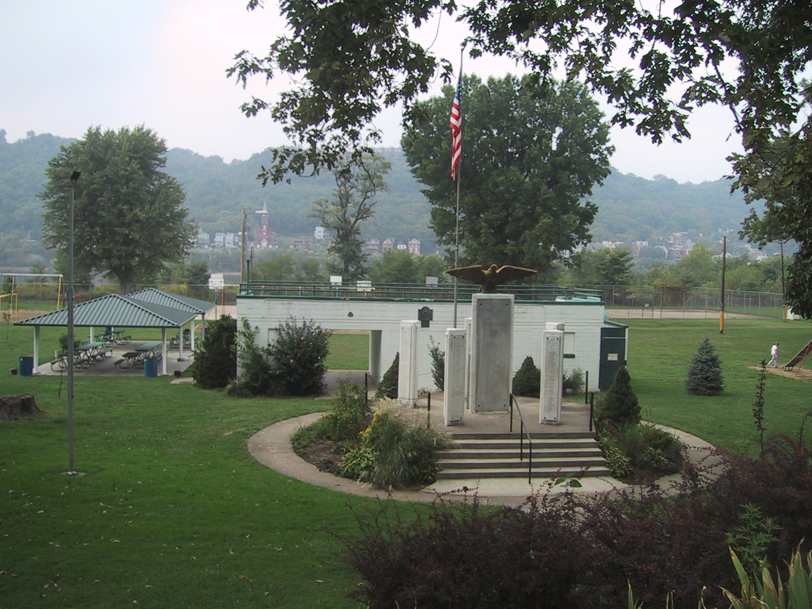 A park with a central war memorial featuring an eagle statue, surrounded by green lawns, picnic shelters, and trees.