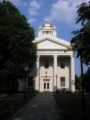 White courthouse with columns and a dome, surrounded by trees, under a partly cloudy sky.