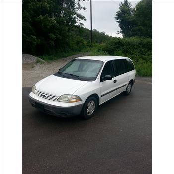 White minivan parked on a paved area with trees and greenery in the background.