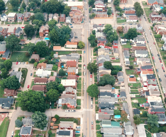 Aerial view of a residential neighborhood with tree-lined streets, single-family homes, intersecting roads, and parked cars arranged in a grid pattern