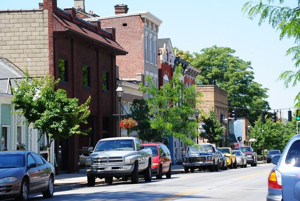 Row of historic brick storefronts along a main street with parked cars and colorful building facades.